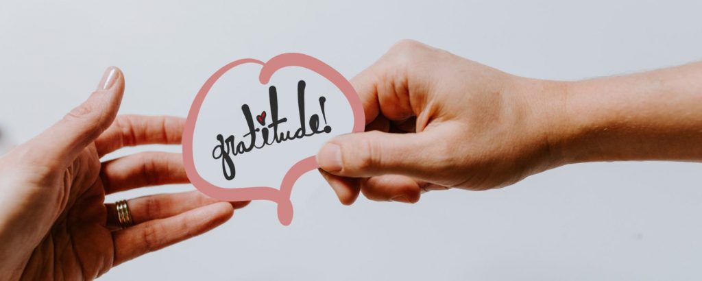 Gratitude Logo being held by the hands of two people.