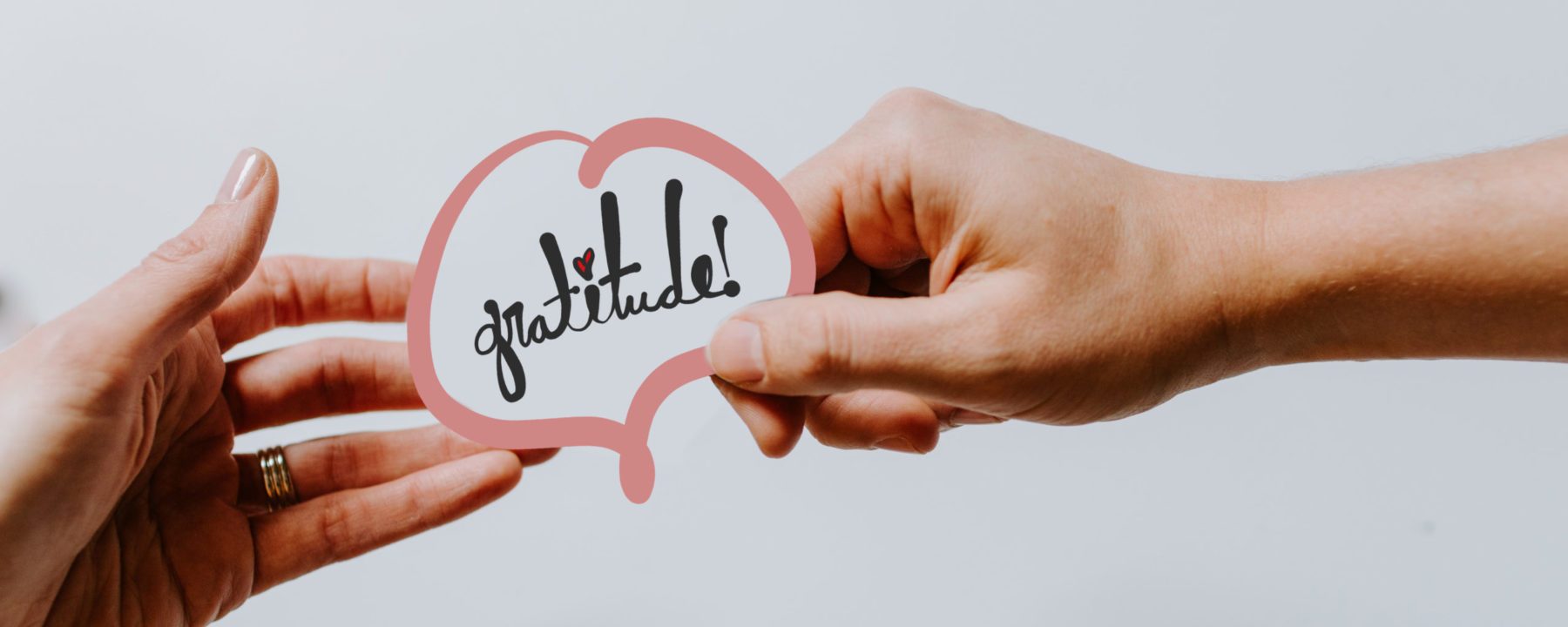 Gratitude Logo being held by the hands of two people.