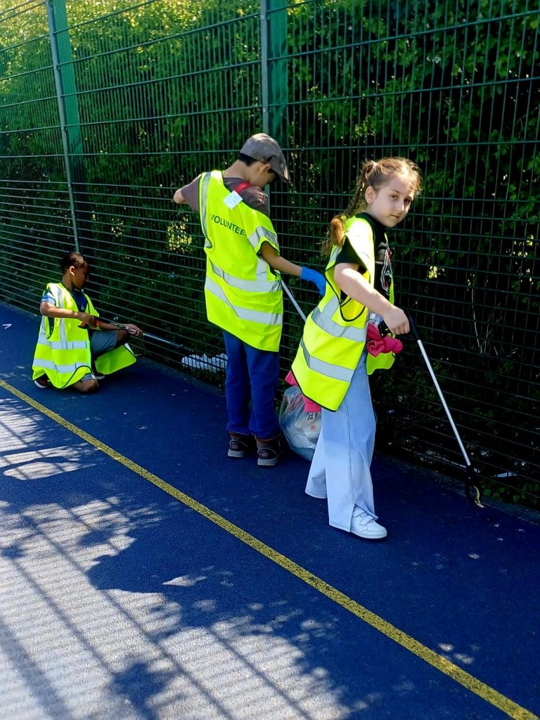 Children volunteers cleaning up with litter pickers and rubbish bags in hi visibility jackets starting the community clean-up