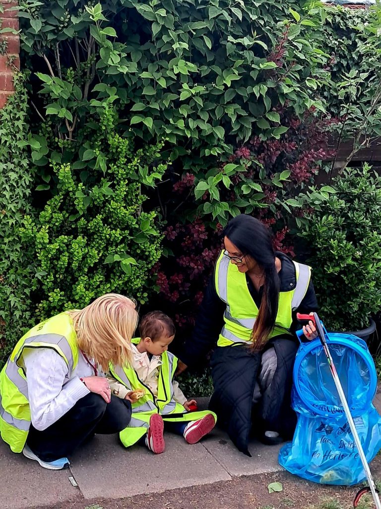 Family volunteers cleaning up with litter pickers and rubbish bags in hi visibility jackets at the community clean-up