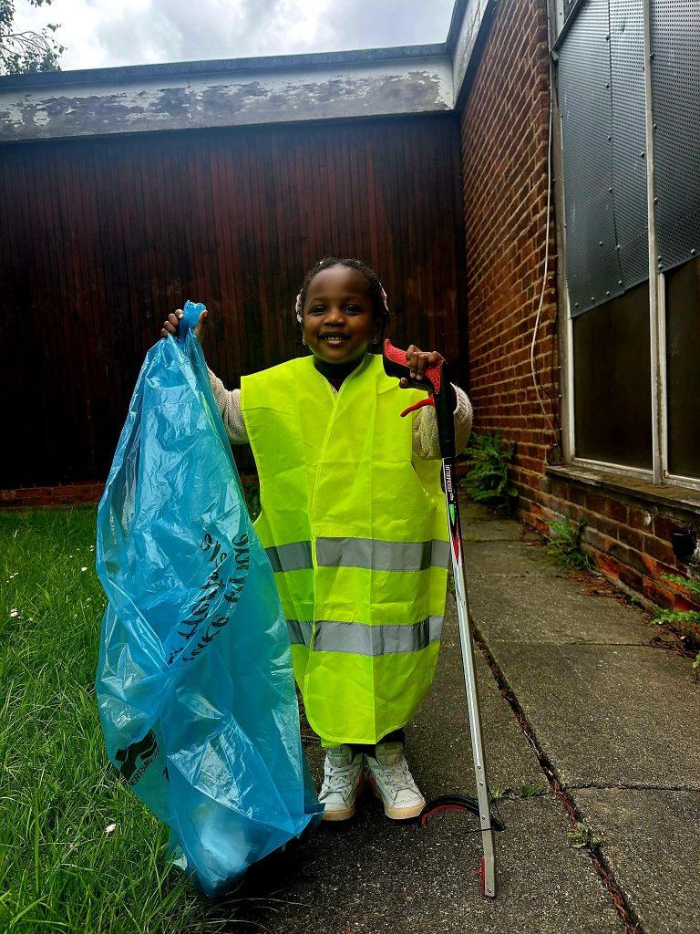 Child volunteer cleaning up with litter picker and rubbish bag ready for the community clean-up
