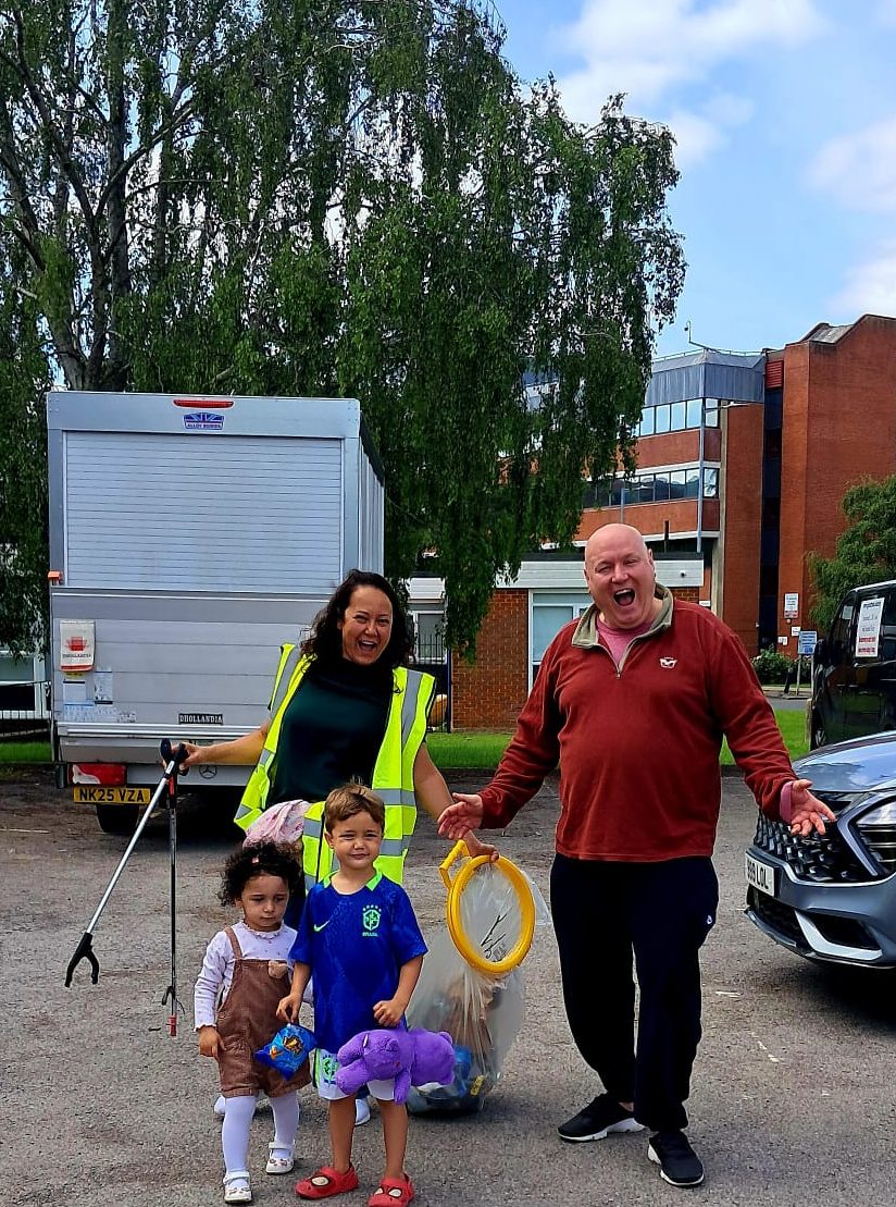 Family volunteers cleaning up with litter pickers and rubbish bags in hi visibility jackets at the community clean-up