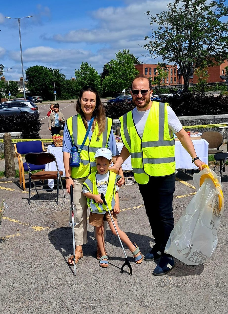 Family volunteers cleaning up with litter pickers and rubbish bags in hi visibility jackets ready for the community clean-up